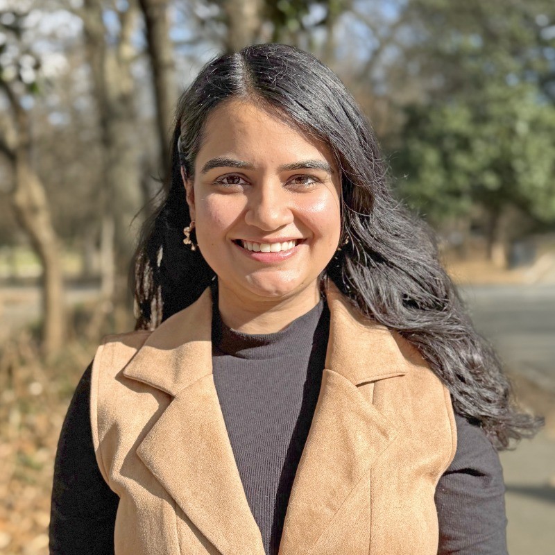 Ritika Narang smiling outdoors in a tan vest